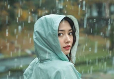 Young woman wearing a light green hooded raincoat looking back in the rain with blurred outdoor background.